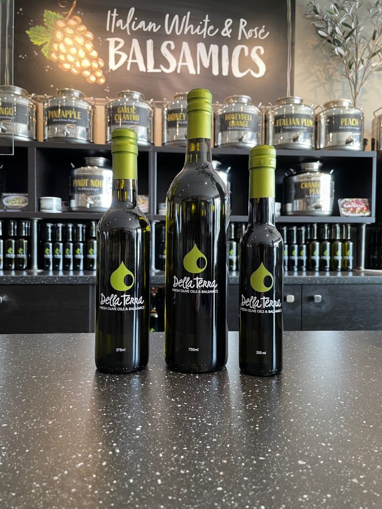 Olive oil and balsamic vinegar glass bottles displayed in front of display shelf in Della Terra Artisanal Olive Oil & Balsamics store.