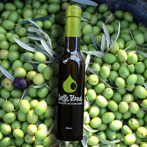 Della Terra Artisan Olive Oil & Balsamics bottle displayed in a bushel of olives.