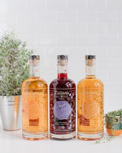 From left to right: Dillon’s 750mL Cassis in between two 750mL Dillon's Peach Schnapps on white countertops surrounded by decorative plants.