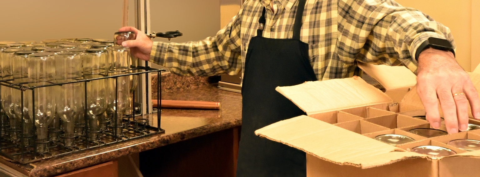 person moving washed glass bottles from wire rack sitting on counter into a box sitting on another counter.